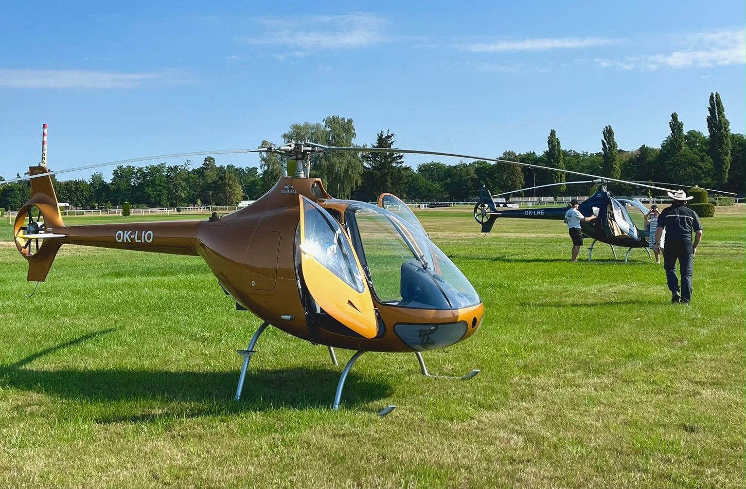 Guimbal Cabri G2 OK-LIO na travnaté ploše s dalšími vrtulníky v pozadí